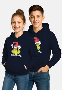Due adolescenti sorridenti indossano felpe blu navy con l'immagine del Grinch in un cappello da Babbo Natale e la scritta "Feelin' Grinchy", mentre stanno in piedi con le mani nelle tasche.
