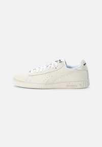 Sneaker en cuir blanc avec un bout arrondi, des détails perforés, des lacets plats blancs et une semelle en caoutchouc texturée blanche. Logo sur la languette et le talon.