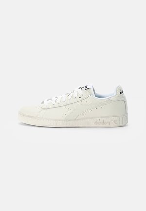 White leather sneaker with a rounded toe, perforated details, flat white laces, and a textured white rubber sole. Logo on tongue and heel.