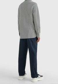 Camisa de botones a rayas en blanco y negro, combinada con pantalones holgados azul marino y zapatillas blancas. Textura de algodón, corte relajado.