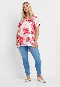 Blommig blus i krämfärgad satin, med stora rosa rosor, korta ärmar och rundad fåll. Bärs tillsammans med ljusblå skinny jeans och silvriga ballerinas.