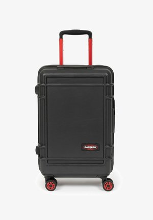Maleta rígida negra con acabado texturizado, ruedas rojas y asa telescópica. Presenta el logo de EASTPAK en la parte frontal y acentos protectores en las esquinas.
