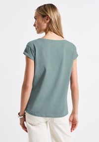Short-sleeve teal shirt made of soft fabric, featuring a relaxed fit with rolled sleeves and a wide neckline. Lightweight and simple design.