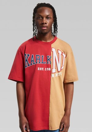 Rød og tan oversized t-shirt med hvid påskrift "KARLK" og "N" på fronten. Bomuldsstof med korte ærmer og rund halsudskæring.