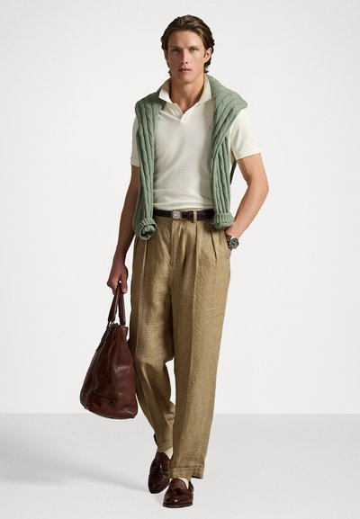 Strikket grønn vest over en hvit polo, kombinert med beige rutete bukser. Brun lær tote og loafers fullfører antrekket. Grønn klokke er synlig.