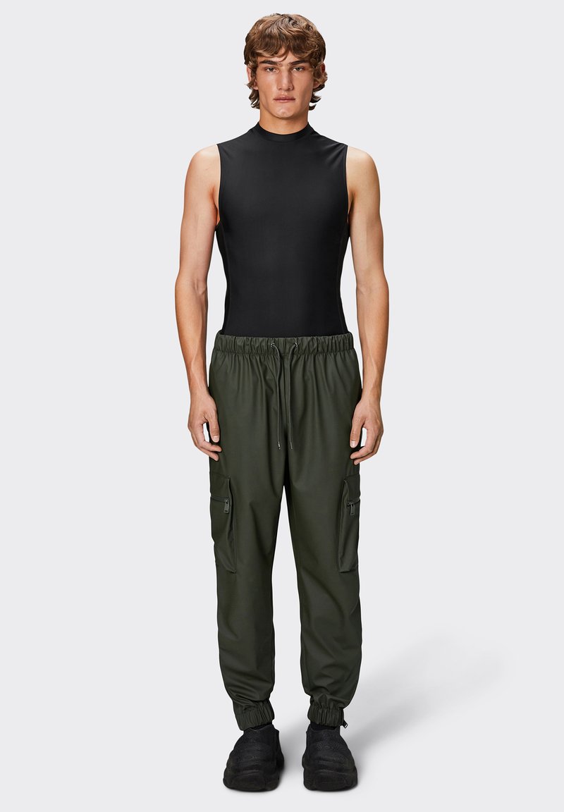 Bodycon senza maniche di colore nero abbinato a jogger cargo larghi di colore verde scuro con tasche con zip e polsini elastici alla caviglia. Scarpe nere.