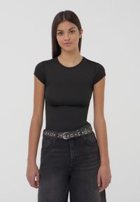 Body nero a maniche corte con scollatura rotonda, realizzato in materiale morbido. Abbinato a jeans neri in denim a vita alta e una cintura borchiata.