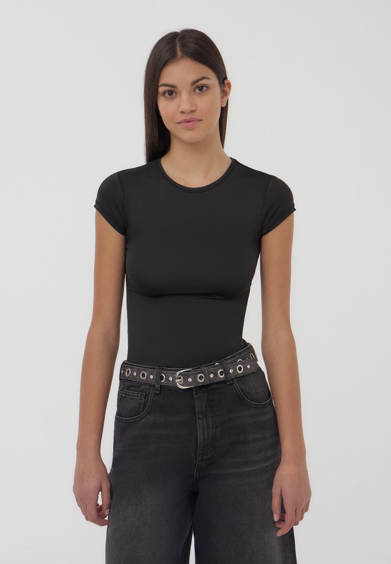 Body nero a maniche corte con scollatura rotonda, realizzato in materiale morbido. Abbinato a jeans neri in denim a vita alta e una cintura borchiata.