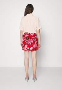 Camicia rosa chiaro a maniche corte abbinata a una mini gonna a fiori rossi. Presenta una fascia elastica in vita e tacchi blu aperti davanti.
