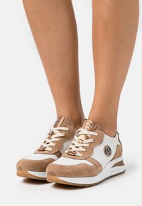 Sneaker leggere con design in suede bianco e beige, dotate di accenti metallici, sistema di allacciatura e tacco testurizzato per una presa migliore.