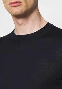 Mörkblå stickad tröja med ribbat runt halsen och en slät yta, har en åtsittande design och minimala sömmar.