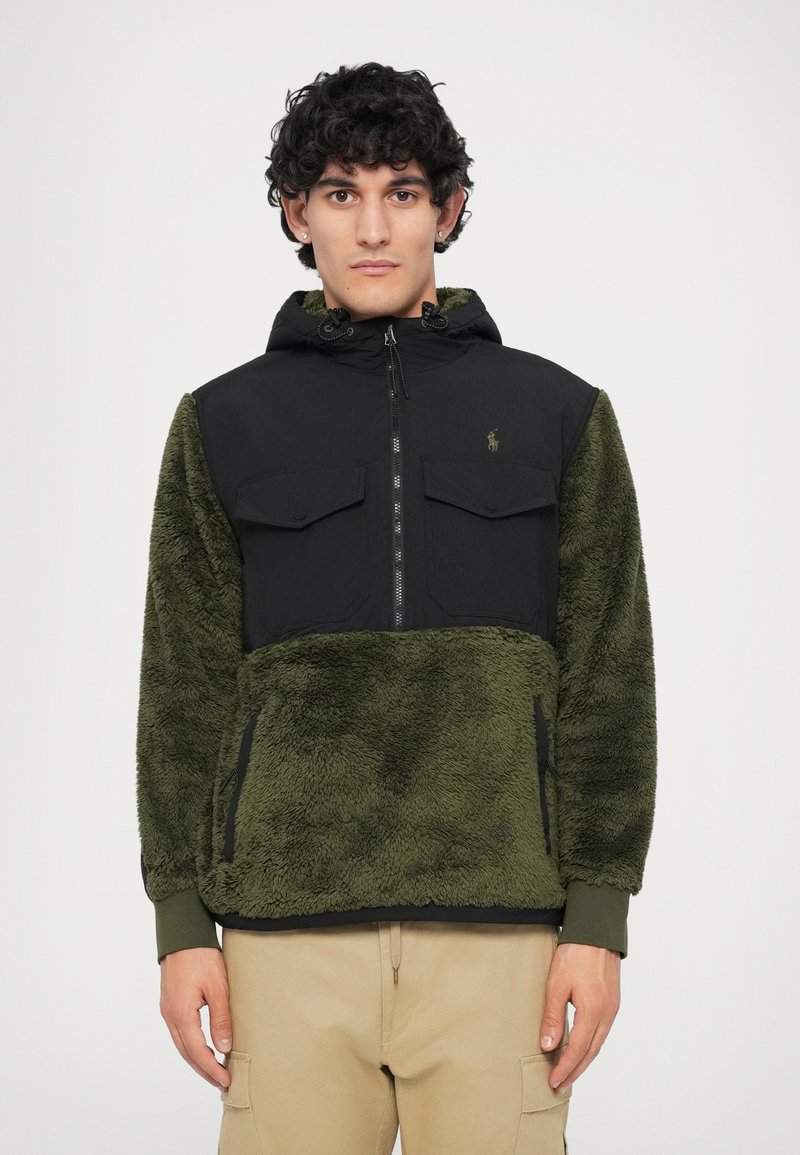 Casaco com capuz em fleece e nylon, verde e preto, com fecho de correr, bolsos no peito e punhos elásticos. Textura suave com um design em contraste.