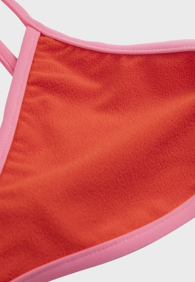 Gros plan sur un tissu polaire rouge avec bordure rose et sangle, montrant la texture douce et les détails de couture.