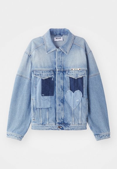 Vaaleansininen farkkutakki, jossa tummansiniset paikat, mukaan lukien sydämenmuotoinen paikka edessä, ja nappisuljenta, asetettuna tasaiseksi.