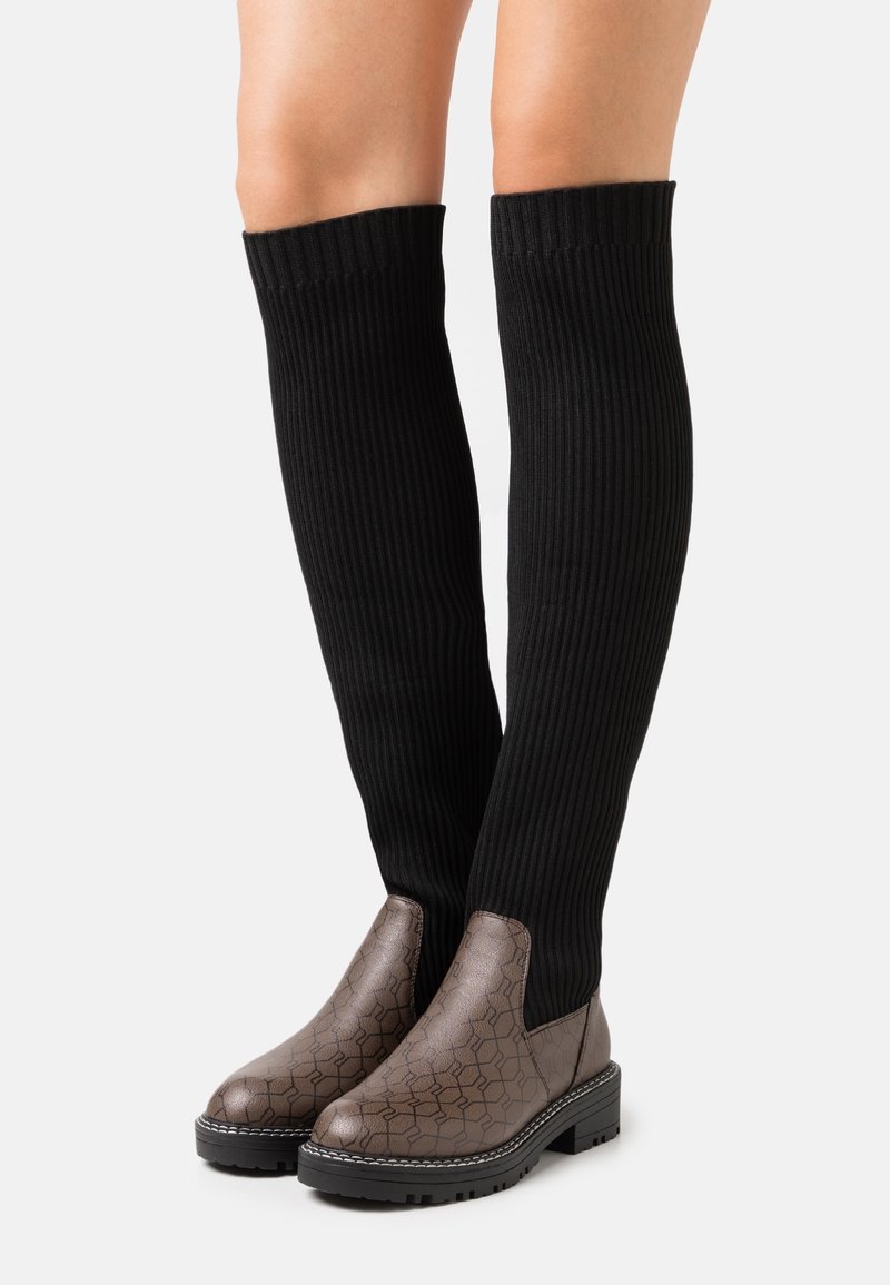 Piernas con calcetas altas de punto acanalado negro combinadas con botines de piel marrón con un estampado, que tienen suelas gruesas.