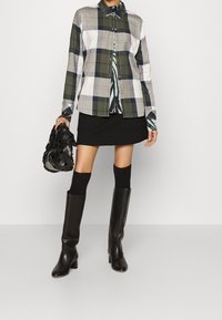 Koszula w kratę w odcieniach zieleni, szarości i bieli, połączona z czarną mini spódnicą. Czarne botki za kolano i fakturowana czarna torba dopełniają całość.