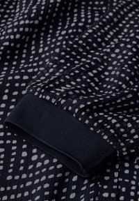 Marineblaue Stoff mit einem strukturierten, gestreiften Muster, das unregelmäßige weiße Punkte aufweist. Ein gerippter Saum am Boden sorgt für einen kontrastierenden Akzent.