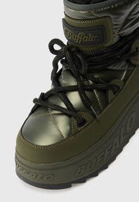 Alyvų žalia kulkšninių botų viršus pagamintas iš blizgaus audinio, storos juodos raišteliai ir guminis padas. Išskirtinis prekės ženklo logotipas ant liežuvėlio ir įspaustas šone.