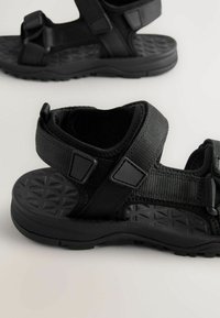 Svart sandal med en strukturerad gummisula, justerbara nylonremmar och plastdetaljer. Har en sportig design för bra grepp och komfort.