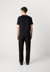 Black short-sleeve t-shirt with a round neckline, paired with black cargo pants featuring side pockets and silver snap buttons.