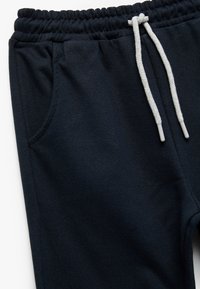 Marineblaue Sweatpants aus weichem Stoff, mit einem elastischen Bund und grauen Kordeln sowie zwei Seitentaschen.