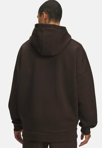 Sweat à capuche marron avec une coupe décontractée, des épaules tombantes et des poignets et un ourlet côtelés. Texture de tissu douce, sans motifs ni accents visibles.