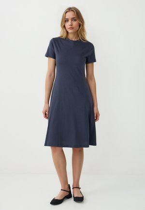Abito in cotone blu navy a maniche corte con scollo rotondo e forma a A, che arriva sopra il ginocchio. Scarpe nere piatte con cinturini.