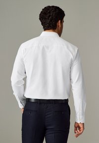 White long-sleeve shirt with a textured pattern, featuring a straight collar and button cuffs, paired with dark pants and a black belt.