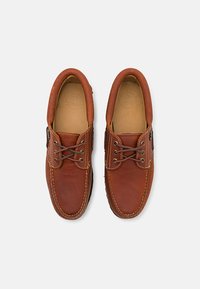 Brown leather shoes with a rounded toe, contrasting stitching, and eyelets for laces. Smooth texture and soft inner lining detail.