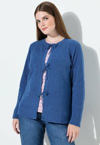 Blauer Strickcardigan mit langen Ärmeln, ausgestattet mit einem runden Ausschnitt und Bänder zum Binden an der Vorderseite. Trägt man über einem rosa-weißen gestreiften Oberteil.