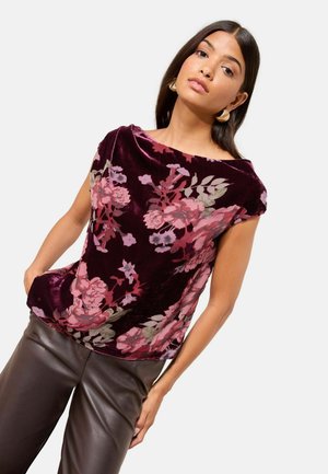 Velvet top in deep burgundy with a floral print featuring pink and green accents; scoop neckline and short sleeves. Paired with brown leather pants.