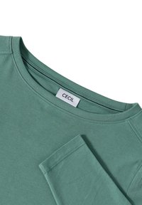 Groen langwerpig T-shirt met lange mouwen, gemaakt van zachte stof, met een ronde halslijn en een label met de tekst "CECIL" aan de binnenkant van de kraag.
