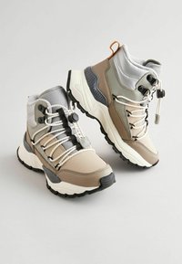 Beige und graue Wanderschuhe mit einem Obermaterial aus strukturiertem Stoff, Gummisohlen, dynamischem Schnürsystem und gepolstertem Kragen für zusätzlichen Komfort.