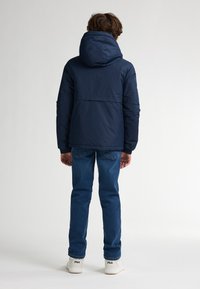 Marineblaues Daunenjacke mit Kapuze, entworfen für Wärme. Verfügt über eine glatte Textur und elastische Bündchen, kombiniert mit blauem Denim und weißen Turnschuhen.