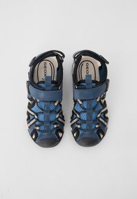 Blå sandaler med nät- och lädermaterial, med en kardborreband och en texturerad sula. Öppen design med randiga mönsterdetaljer.