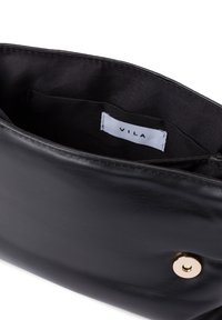 Bolso de mano de cuero negro con una textura suave, cierre a presión dorado y bolsillo interior. La etiqueta dice "VILA" en una etiqueta de tela.