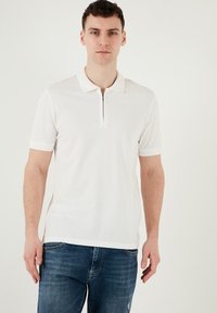 Vit kortärmad polo-shirt i slät tyg, med dragkedja i kragen och texturerade detaljer på ärmarna.