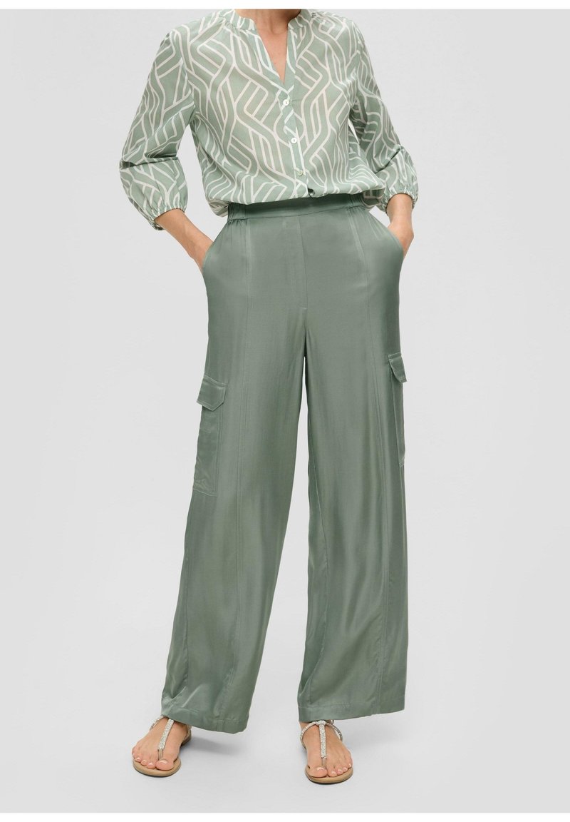 Ljusgrön mönstrad blus med knapppdetaljer, tillsammans med vida gröna satinbyxor med sidofickor och en slät yta.