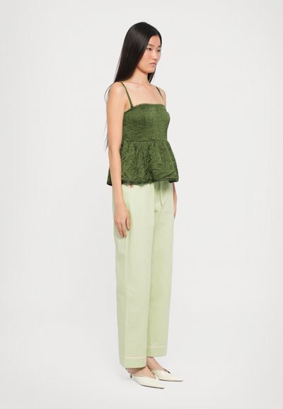 Green textured peplum top with thin straps, paired with light green wide-leg trousers, and pale shoes. Simple and contemporary design.