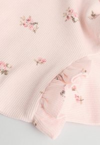 Hellrosa gerippter Stoff mit kleinen Blumenmustern in Pink und Grün. Der Rüschensaum verleiht dem Design Textur und Detail.