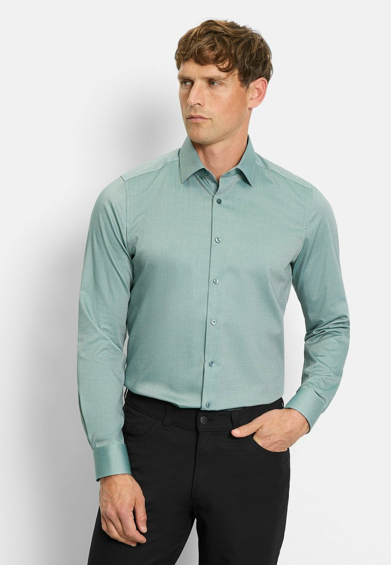 Hellgrünes Langarmhemd mit spitzem Kragen, knöpfbare Vorderseite und dezentem Texturmuster, kombiniert mit schwarzen Hosen.