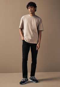 Beiges kurzärmliges T-Shirt, schwarze Slim-Fit-Jeans und dunkle Sneaker mit weißen Akzenten. Glatte Textur, lockere Passform, modernes Design.