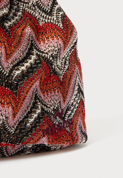 Woven bag featuring a zigzag pattern in red, pink, silver, and black. Shiny threads add texture, with branding discreetly visible.