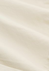 Tissu en coton ivoire avec une texture lisse, présentant de légères rides et un tombé doux, adapté pour les vêtements ou les textiles d'intérieur.