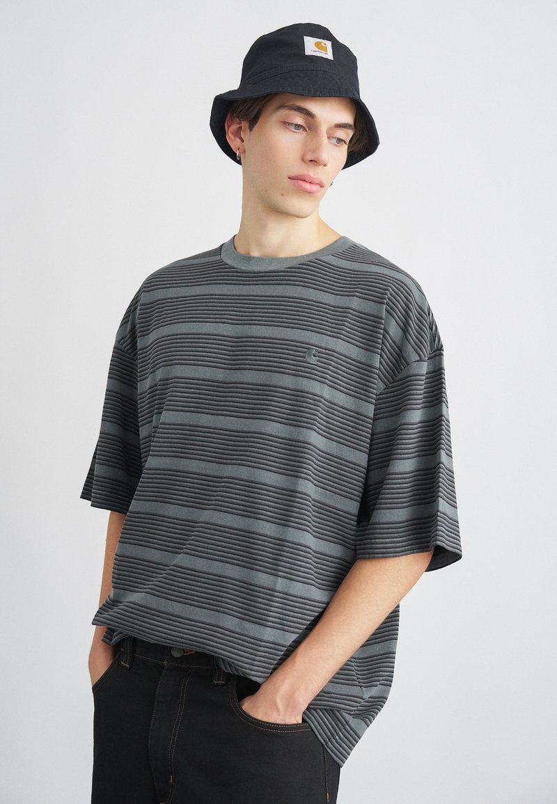 Szara, w paski koszulka z krótkim rękawem wykonana z bawełny, z poziomą teksturą prążkowaną i małym logo na klatce piersiowej. Czarny kapelusz typu bucket.