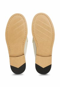 Schoenzolen met een tan leren basis, voorzien van horizontale ribbels, zwarte rubberen accenten bij de hak en gestikte details langs de rand.