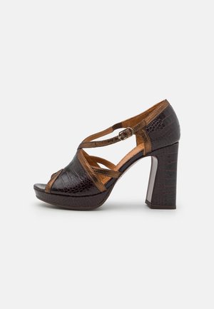 Brown high-heeled sandal with a crocodile texture, featuring an open toe and crisscross straps. The heel is a solid block design.