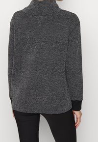 Pullover strutturato in nero e grigio con colletto alto, dotato di maniche lunghe e polsini neri, progettato per una vestibilità comoda.