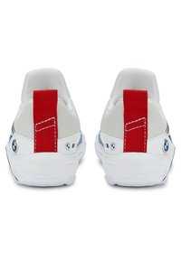 Vita canvas sneakers med en röd dragtab, blå accenter och en framträdande logodetalj nära hälena. Platta gummisulor, sydda detaljer.