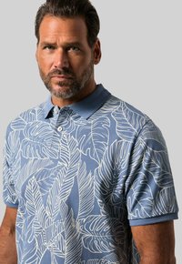 Světle modré polo tričko s bílým listovým vzorem, krátké rukávy a límeček. Obsahuje dvouknoflíkovou légu a strukturovanou tkaninu.